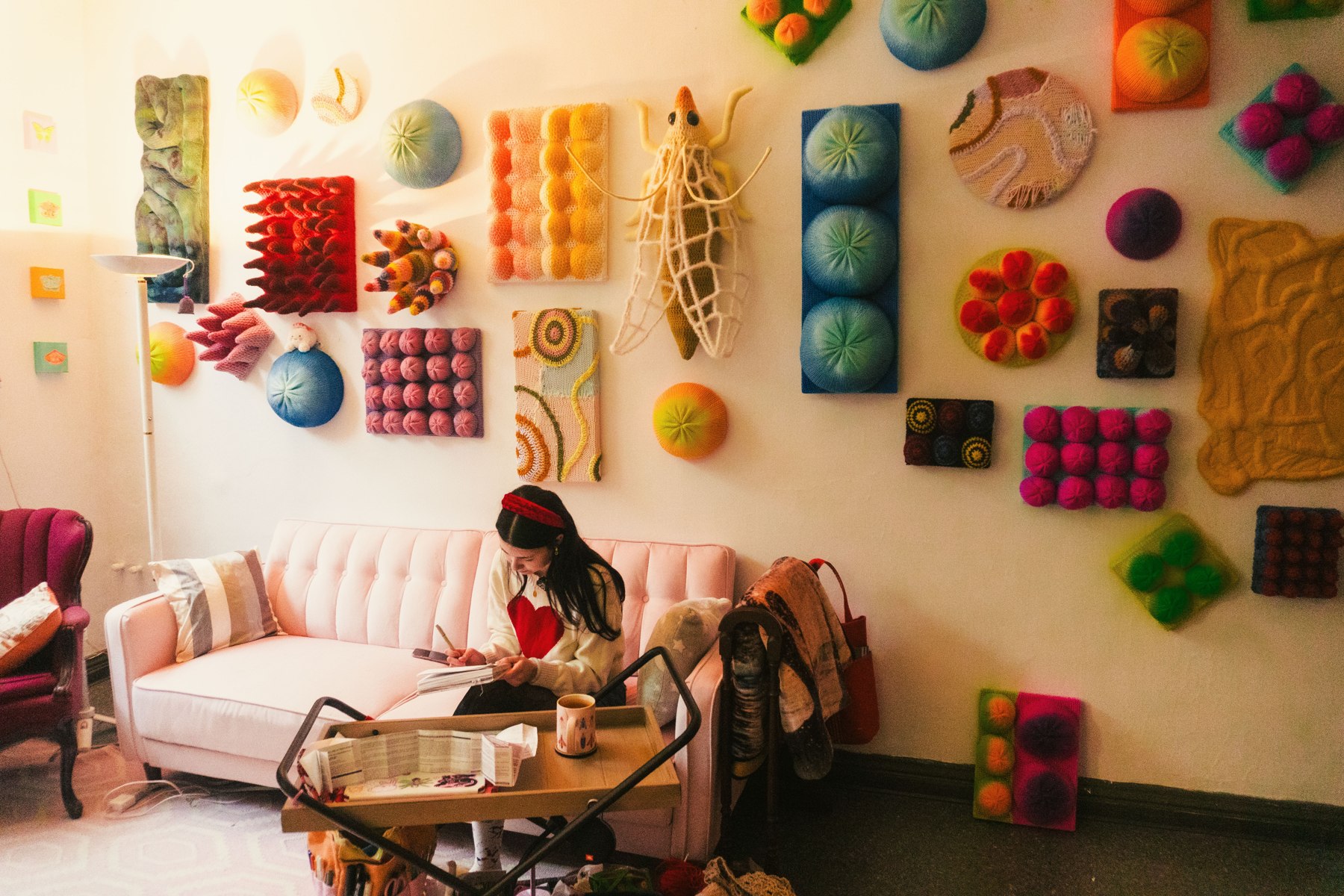 An artist working on a pink sofa beneath colourful textile artwork